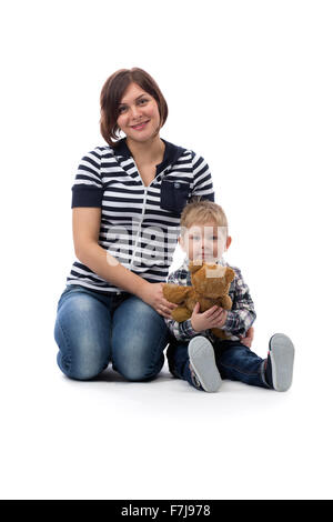 Young beautiful mother in blue jeans sitting with her son three years on the floor in the studio, isolate on white. Stock Photo