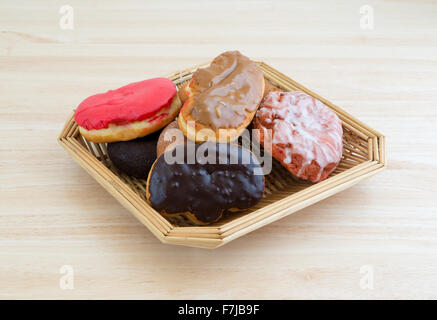 An old wicker basket filled with assorted donuts and iced cherry fritter on a wood table top illuminated with natural light. Stock Photo
