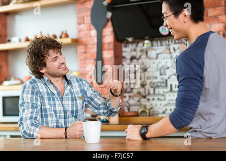 Group of two excited cheerful young guys sitting, talking and laughing in student cafe Stock Photo
