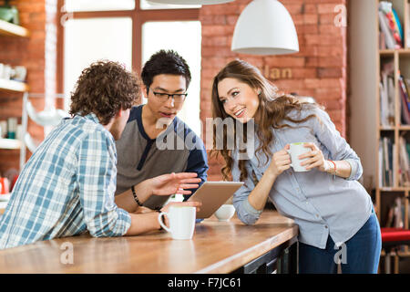 Group of joyful positive students talking and using laptop in cafe Stock Photo