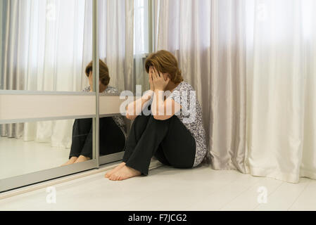 Woman with depression sitting in  corner of the room Stock Photo