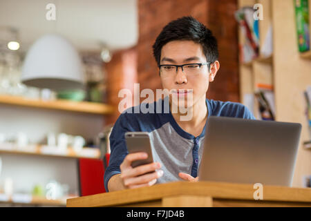 Thoughtful serious asian man using smartphone and laptop in cafe Stock Photo