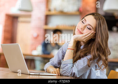 Attractive relaxed curly young woman sitting in cafe with closed eyes, smiling and dreaming Stock Photo