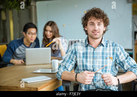 Attractive cheerful young curly male in checkered shirt studying with students in classroom Stock Photo