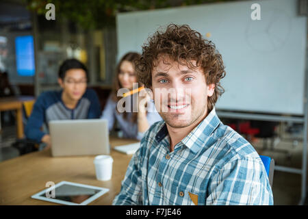Handsome positive young curly man in plaid shirt sitting and studying together with friends Stock Photo