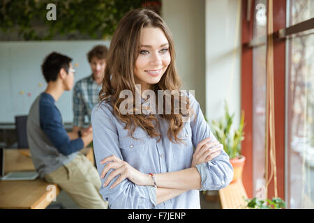 Happy beautiful young female looking at the window with folded hands and with her friends on background Stock Photo