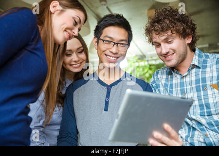Joyful smiling young friends holding and using tablet Stock Photo