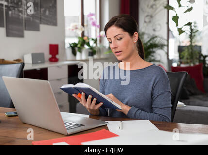 Frau zuhause, sitzt an Schreibtisch mit Laptop und Kalender Stock Photo
