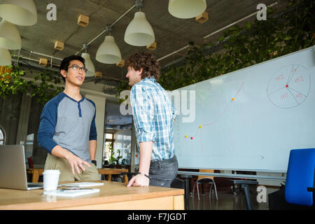 Positive confident young male students standing and talking in classroom Stock Photo