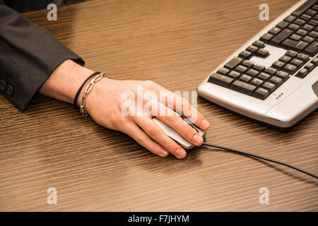 Hand of a man working at computer clicking on mouse in his office, on dark desktop Stock Photo