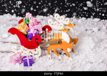 closeup of Christmas decoration reindeer and Santa sleigh with presents in traces snow on black background Stock Photo