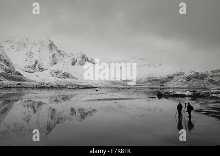 Photographers below snow covered mountains and calm bay, Norway Stock Photo