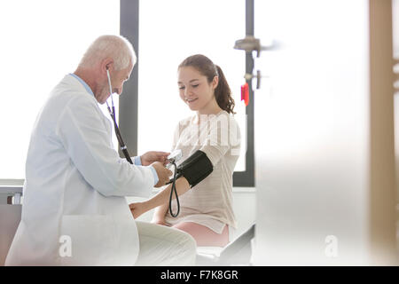Doctor checking teenage patient’s blood pressure with cuff in examination room Stock Photo