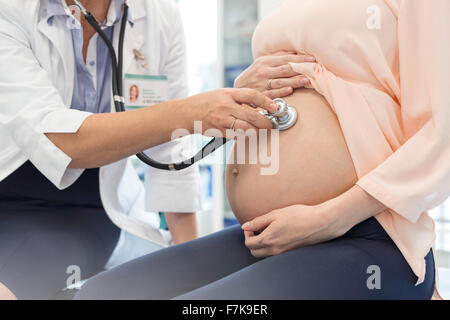Doctor using stethoscope on pregnant patient’s stomach Stock Photo