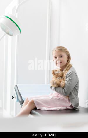 Portrait smiling girl patient hugging teddy bear in examination room Stock Photo