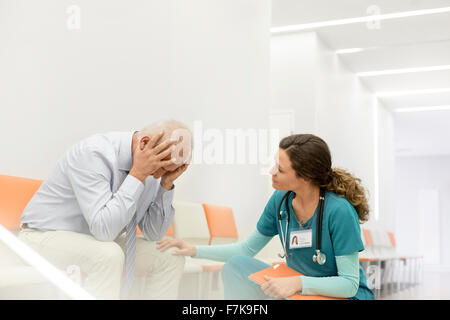 Nurse consoling upset man in clinic corridor Stock Photo