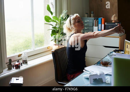 Young woman stretching arms at desk in home office Stock Photo