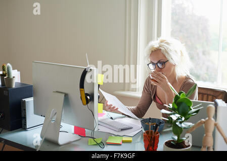 Young woman drinking tea and reading paperwork at desk in home office Stock Photo