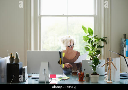 Young woman reading paperwork at desk in home office Stock Photo