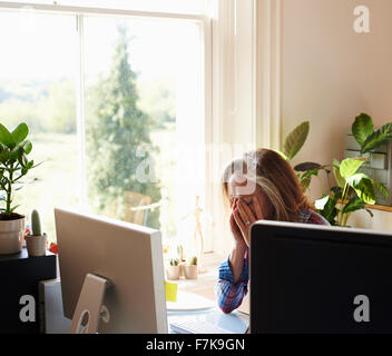 Tired woman with head in hands at computer in home office Stock Photo