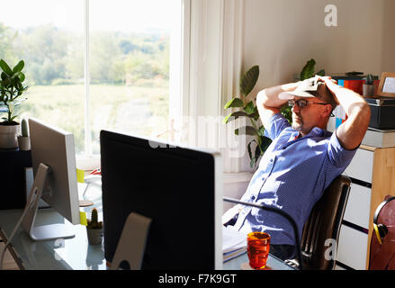 Man leaning back working at computer in sunny home office Stock Photo