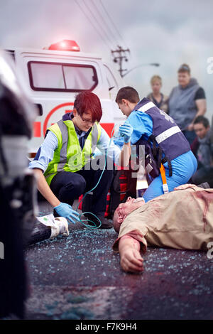 Rescue workers tending to car accident victim in road Stock Photo