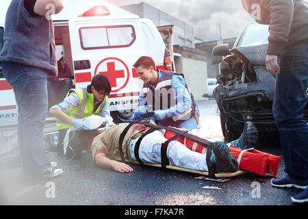 Rescue workers tending to car accident victim in road Stock Photo