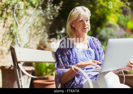 Senior woman using laptop on sunny garden bench Stock Photo