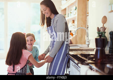 Mother and daughters holding hands in kitchen Stock Photo