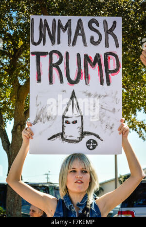 An attractive young female protester holds a handmade sign with KKK character reads Unmask Trump at Donald Trump political rally Stock Photo