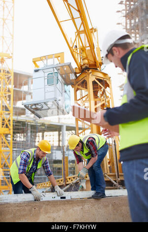 Construction workers using level tool below crane at construction site Stock Photo