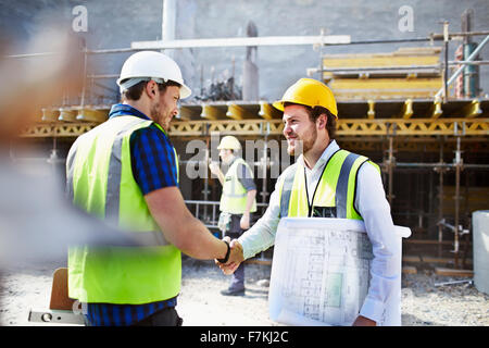 Construction worker and engineer with blueprints handshaking at construction site Stock Photo