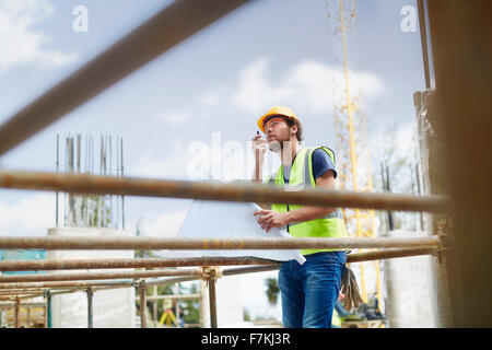 Engineer with blueprints using walkie-talkie at construction site Stock Photo