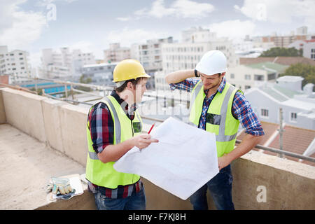 Construction worker and engineer reviewing blueprints at highrise construction site Stock Photo