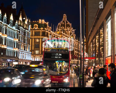 CHRISTMAS TRAFFIC TAXI ULEZ SHOPPERS  Harrods department store at night with lit 'Sale' sign shoppers red bus, busy traffic Knightsbridge London SW1 Stock Photo