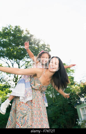 Portrait carefree mother piggybacking daughter with arms outstretched Stock Photo