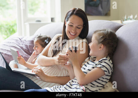 Mother and daughters with cell phone, laptop and digital tablet on sofa Stock Photo