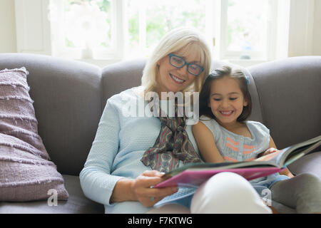 Grandmother and granddaughter reading book on living room sofa Stock Photo
