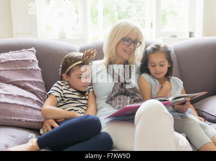 Grandmother and granddaughters reading book on living room sofa Stock Photo