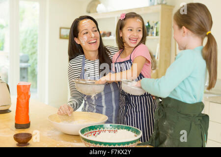 Laughing mother and daughters baking with flour on faces in kitchen Stock Photo