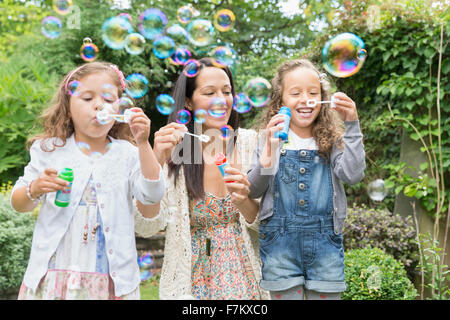 Mother and daughters blowing bubbles in backyard Stock Photo