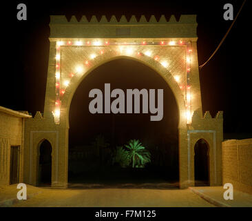 A lighted gate at night leads to the main Palmeraie in Tozeur. A palm tree is illuminated in the distance. Tozeur, Tunisia. Stock Photo