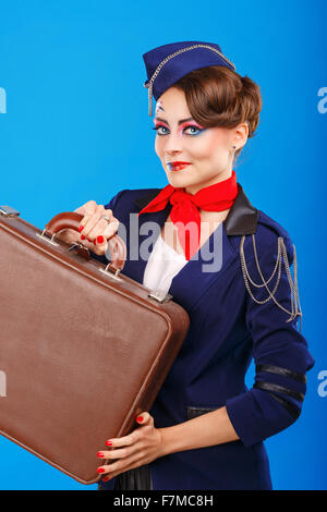 Stewardess with face art holds suitcase. Young attractive girl in a blue suit flight attendants. Airfreight. Service. Baggage. Stock Photo