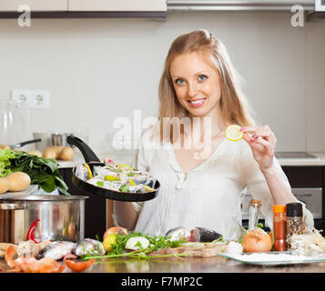 Smiling girl cooking fish with lemon in frying pan at  kitchen Stock Photo