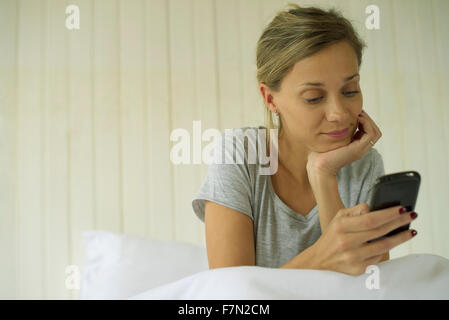 Woman sitting in bed using smartphone Stock Photo