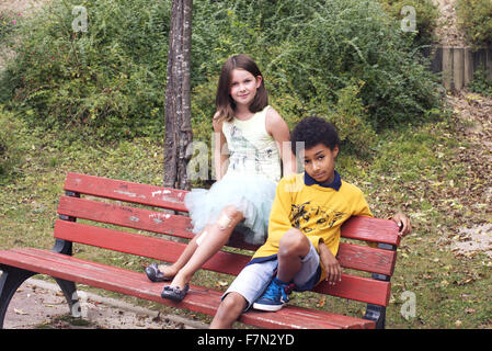 Children sitting together on park bench Stock Photo