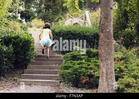 Girl in tutu running up stairs in park, rear view Stock Photo