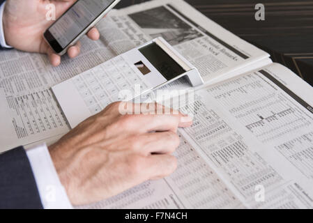 Checking stock market performance using smartphone and newspaper Stock Photo