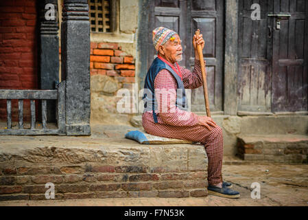 Elderly beggar with a walking stick sits in the street of Kathmandu Stock Photo
