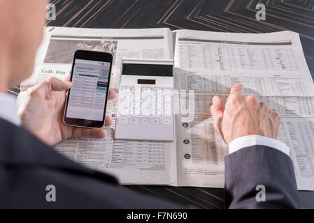Using smartphone and newspaper to monitor stock performance Stock Photo